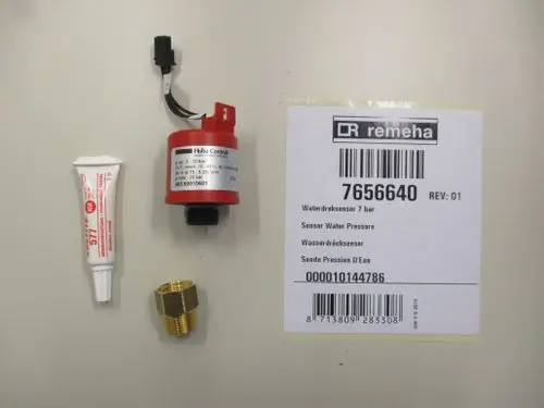 Remeha Wasserdrucksensor mit Anschluss, einer Montagepaste und einer Metallverbindung, auf einem hellen Hintergrund. Verpackung mit Artikelnummer und weiteren Informationen ist sichtbar.